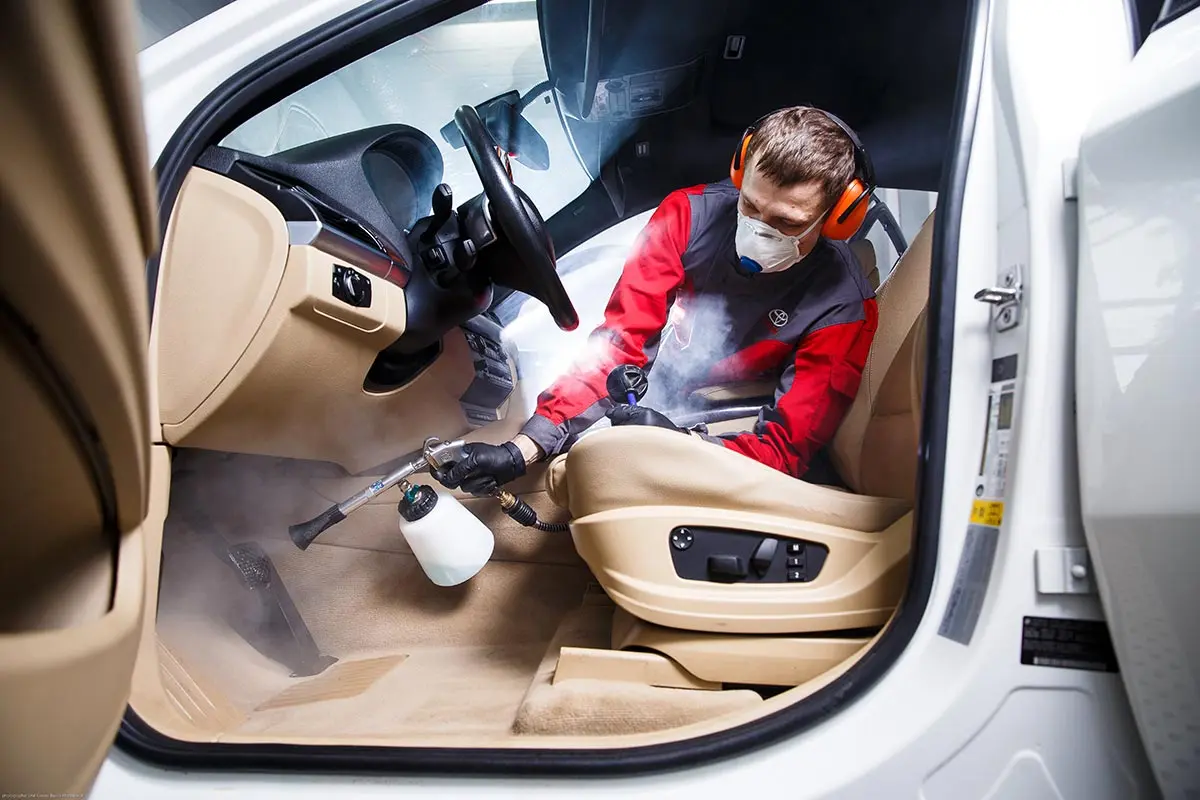 tehnician care curăță interiorul unei mașini cu aspirator și soluții profesionale, bord și scaune bine iluminate